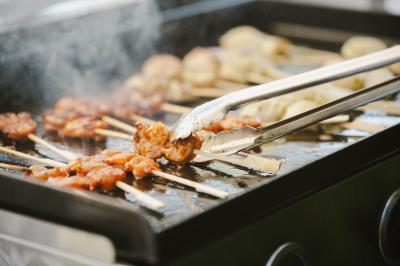 Brochettes de crevettes et autres aliments grillés sur une plancha, avec des pinces en métal manipulant une brochette.