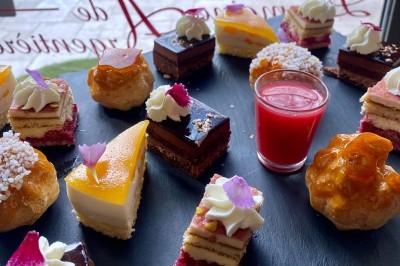Assortiment de pâtisseries miniatures sur un plateau noir, avec une verrine de coulis rouge au centre.