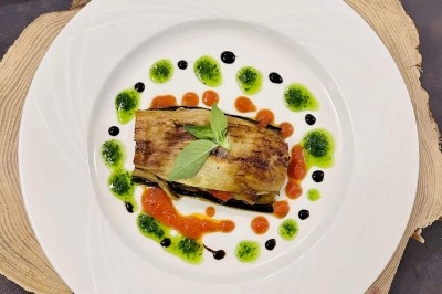 Assiette garnie d'un plat à base d'aubergine grillée, décorée de sauces colorées et d'une feuille de basilic.