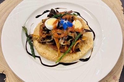Tartelette garnie de légumes grillés, œufs de caille, asperges et sauce balsamique, servie sur une assiette blanche.