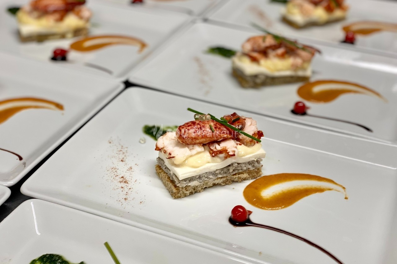 Assiette gastronomique avec une entrée composée de morceaux de homard, mousse, pain, et décorations de sauces colorées.