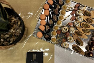 Plateau de bouchées apéritives variées disposées sur des cuillères et des supports en bois, avec une plante en arrière-plan.