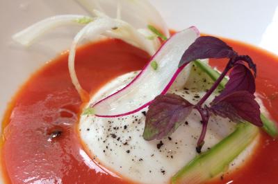 Burrata servie sur un coulis de tomate, garnie de radis, asperges, herbes fraîches et poivre moulu.