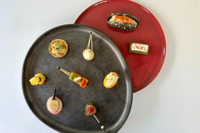 Assortiment de bouchées apéritives variées présentées sur des assiettes noire et rouge.