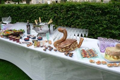 Table dressée en extérieur avec verres, bouteilles, pains, amuse-bouches et desserts sur une nappe blanche.
