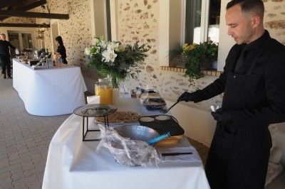 Traiteur Eclat des Saveurs Marles-en-Brie #2 Un cuisinier prépare des crêpes sur une plaque chauffante lors d'un buffet en extérieur près d'un bâtiment en pierre.