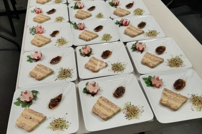 Assiettes dressées avec terrine, sauce, germes et décoration florale en cuisine collective.