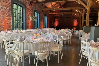 Traiteur France Evenement Traiteur Comines #3 Salle de réception avec tables rondes dressées, chaises blanches et éclairage chaleureux dans un bâtiment en briques.