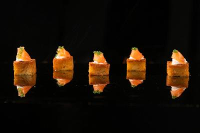 Traiteur Gaudefroy Receptions Ollioules #4 Cinq bouchées apéritives alignées, composées de pain doré, saumon fumé et garniture verte, sur fond noir.