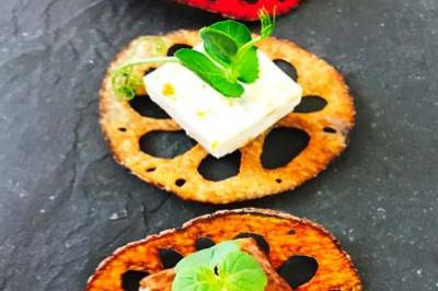 Tranches de lotus colorées garnies de fromage, viande et herbes fraîches, disposées sur une ardoise noire.