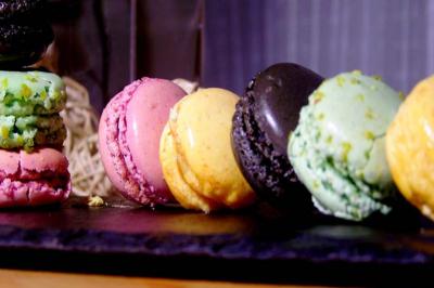 Assortiment de macarons colorés alignés sur une ardoise noire, avec un fond flou et des tons chaleureux.