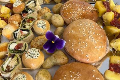 Assortiment de bouchées apéritives variées avec pains, roulés, brochettes de fruits et une fleur comestible violette.
