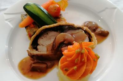 Plat composé d'un filet de viande en croûte, purée décorée, légumes et sauce servie dans une assiette blanche.
