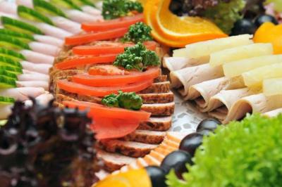Plateau de charcuterie et légumes avec tranches de pain, tomates, concombres, salades, oranges et ananas.
