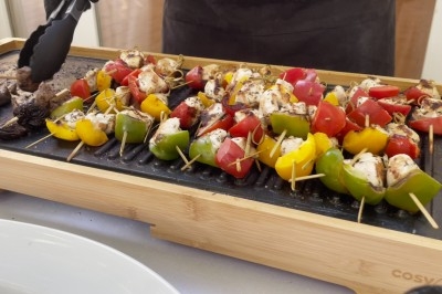 Traiteur Rousseau Traiteur Azay-le-Rideau #3 Brochettes de légumes et de poulet grillées sur une plancha en bois, avec des pinces tenant un morceau.
