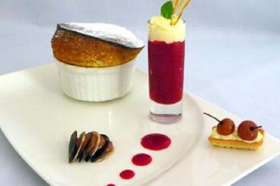Assiette gastronomique avec soufflé, verrine de coulis rouge, noix, cerises et décoration soignée.