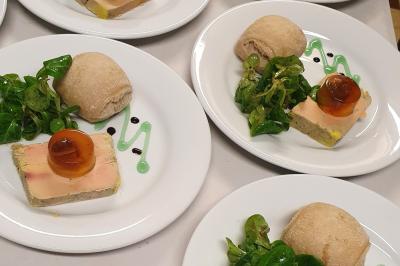 Assiette composée de foie gras, gelée, salade verte, sauce décorative et petit pain.