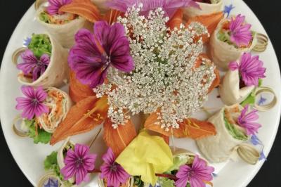 Assiette garnie de rouleaux de légumes frais décorés de fleurs comestibles colorées sur fond noir.