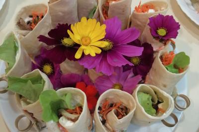 Plateau de wraps garnis de légumes frais, décoré de fleurs comestibles colorées au centre.