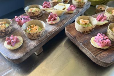 Plateaux en bois garnis de bouchées apéritives colorées, dont des tartinades roses et des crevettes sur des bases…