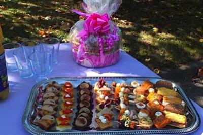 Traiteur Sandrine Traiteur Asnières-sur-Oise #3 Plateau de petits fours variés sur une table violette en extérieur, avec un panier cadeau en arrière-plan.