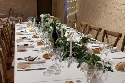 Table de réception décorée avec des fleurs blanches et vertes, bougies et vaisselle élégante dans une salle en pierre.