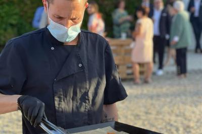 Un cuisinier masqué prépare des aliments sur une plancha lors d'un événement en extérieur.