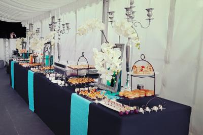 Traiteur Rubis Receptions Magny-le-Hongre #3 Buffet élégant avec nappes noires, décorations florales blanches et chandeliers, proposant divers plats et amuse-bouches.