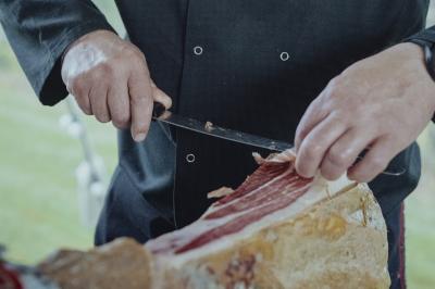 Un cuisinier découpe finement une tranche de jambon cru à l'aide d'un couteau.