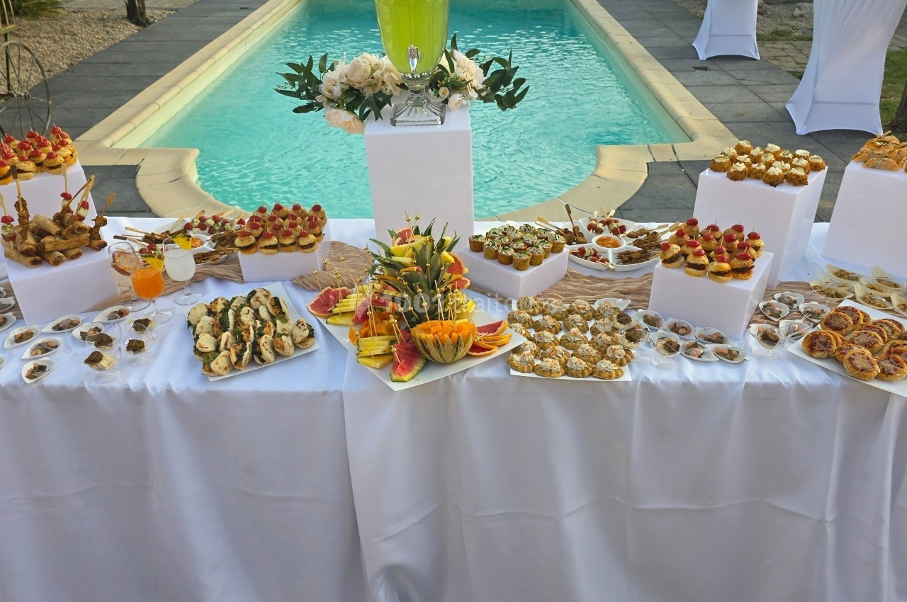Traiteur Royal Events Traiteur et Tradition Saint-Cyr-en-Val #1 Buffet de desserts variés et colorés disposés sur une table blanche près d'une piscine extérieure.