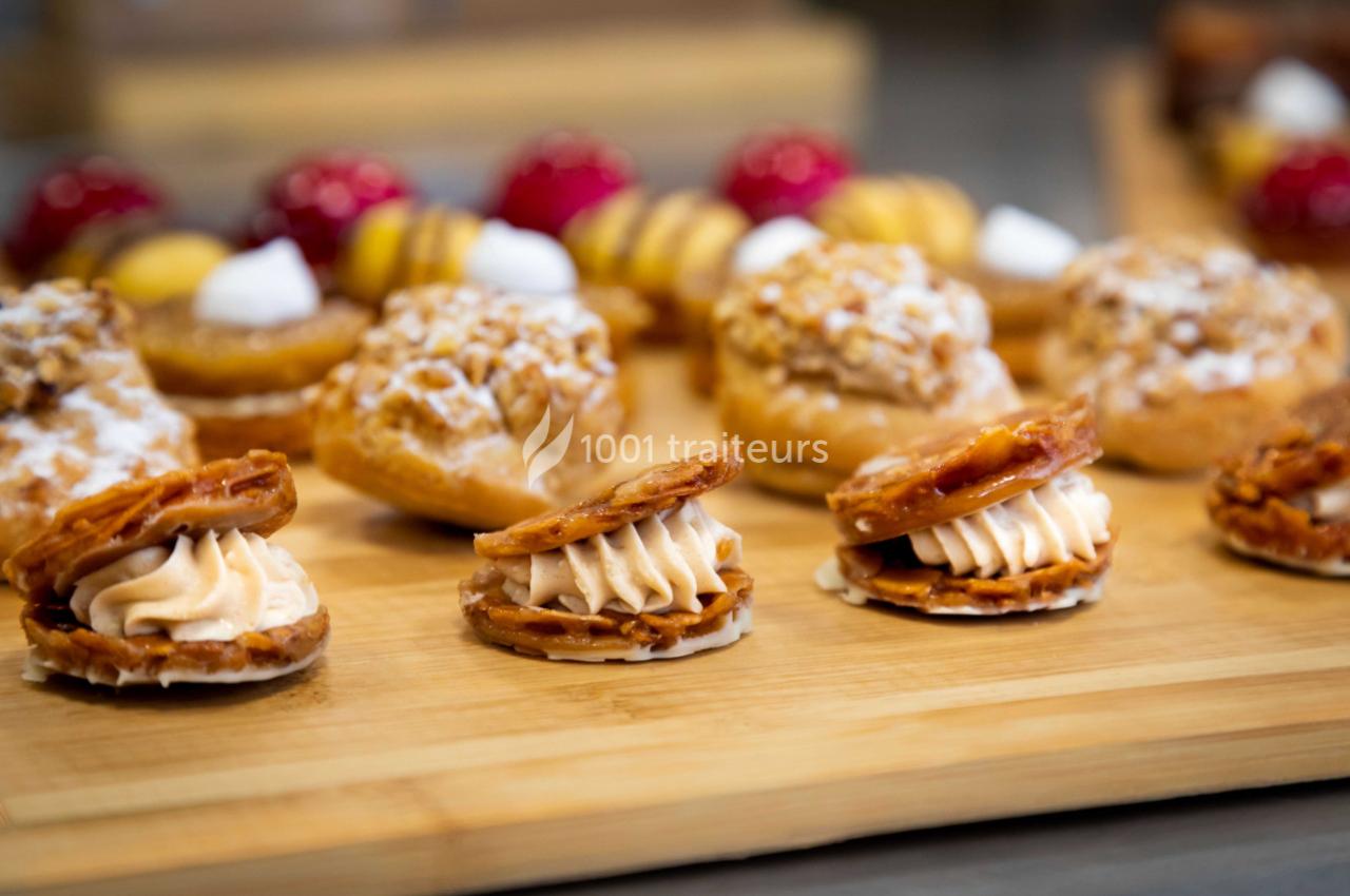 Assortiment de pâtisseries sur une planche en bois, comprenant choux, biscuits garnis et desserts colorés en arrière-plan.