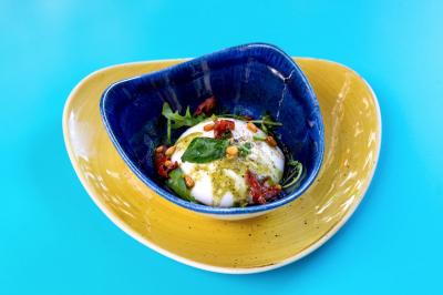Traiteur Maison Tess Traiteur Paris 17 #5 Assiette colorée contenant une burrata garnie de pesto, tomates séchées, pignons de pin et roquette sur fond bleu.