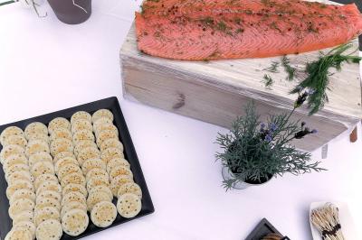 Traiteur Maison Tess Traiteur Paris 17 #4 Saumon gravlax sur planche en bois avec un plateau de blinis et des herbes fraîches en décoration.