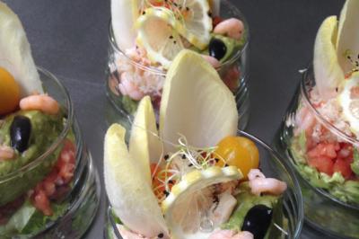 Verrines garnies de crevettes, avocat, tomates, endives, citron, olives noires et germes, présentées sur une table.