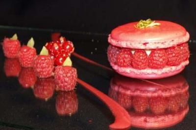 Macaron rose garni de framboises fraîches, accompagné de framboises et groseilles disposées sur une surface noire.