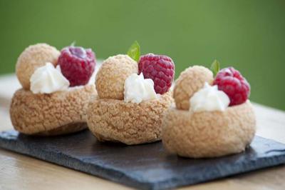 Choux garnis de crème, décorés de framboises et feuilles vertes, présentés sur une ardoise noire.
