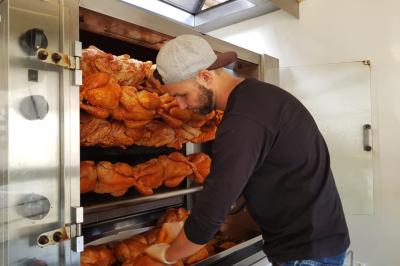Un homme vérifie des poulets rôtis disposés sur des broches dans un four professionnel.