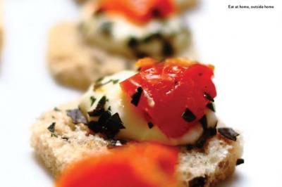 Traiteur Sarah Lima Traiteur Brésilien Élancourt #4 Tranches de pain garnies de fromage fondu, tomates et herbes, présentées en gros plan sur une table.