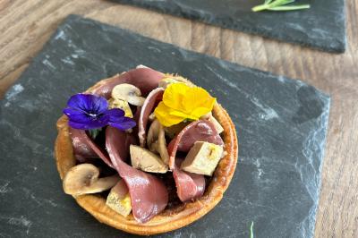 Deux tartelettes garnies de magret de canard, champignons, fleurs comestibles et brins de romarin sur ardoises noires.