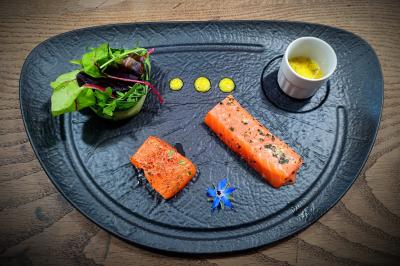 Assiette gastronomique avec saumon mariné, salade verte, sauce en verrine et décoration florale sur une table en bois.