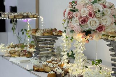Buffet décoré avec des fleurs blanches et roses, présentant des pâtisseries et amuse-bouches sur des présentoirs élégants.