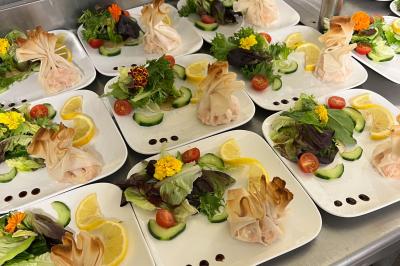 Assiettes dressées avec des aumônières dorées, salade verte, rondelles de concombre, tomates cerises et tranches de citron.