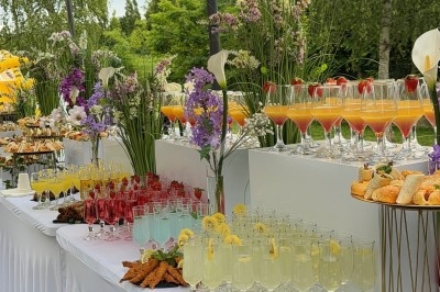 Buffet en plein air avec cocktails colorés, brochettes, fleurs décoratives et desserts sur des tables drapées de blanc.