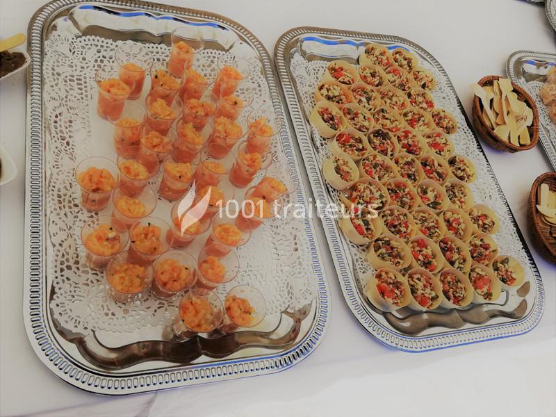 Plateaux de verrines de crevettes et bouchées garnies de légumes colorés, disposés sur des nappes blanches.