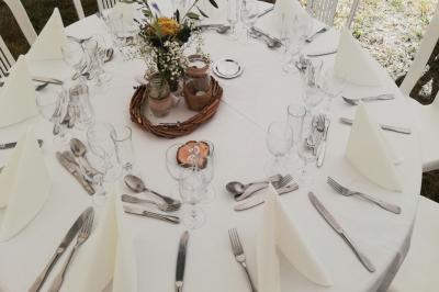 Table ronde dressée avec nappes blanches, couverts, serviettes pliées, verres et centre de table floral.