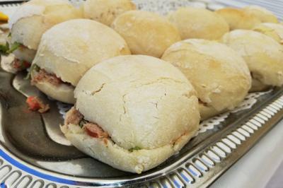 Plateau de petits pains garnis de légumes et de viande, disposés sur une nappe blanche.