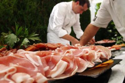 Plateau de charcuterie avec tranches de jambon et garnitures, préparé par deux chefs en arrière-plan.