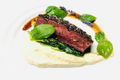 Tranche de viande grillée sur lit d'épinards, purée crémeuse, feuilles de basilic et sauce décorative.