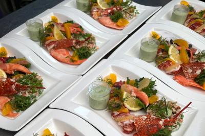 Assiettes de fruits de mer avec homard, saumon, agrumes, salade verte et sauce servies sur des plateaux blancs.