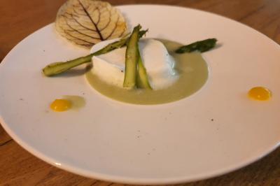 Assiette contenant une mousse blanche sur une sauce verte, garnie d'asperges, d'une feuille et de points de purée jaune.